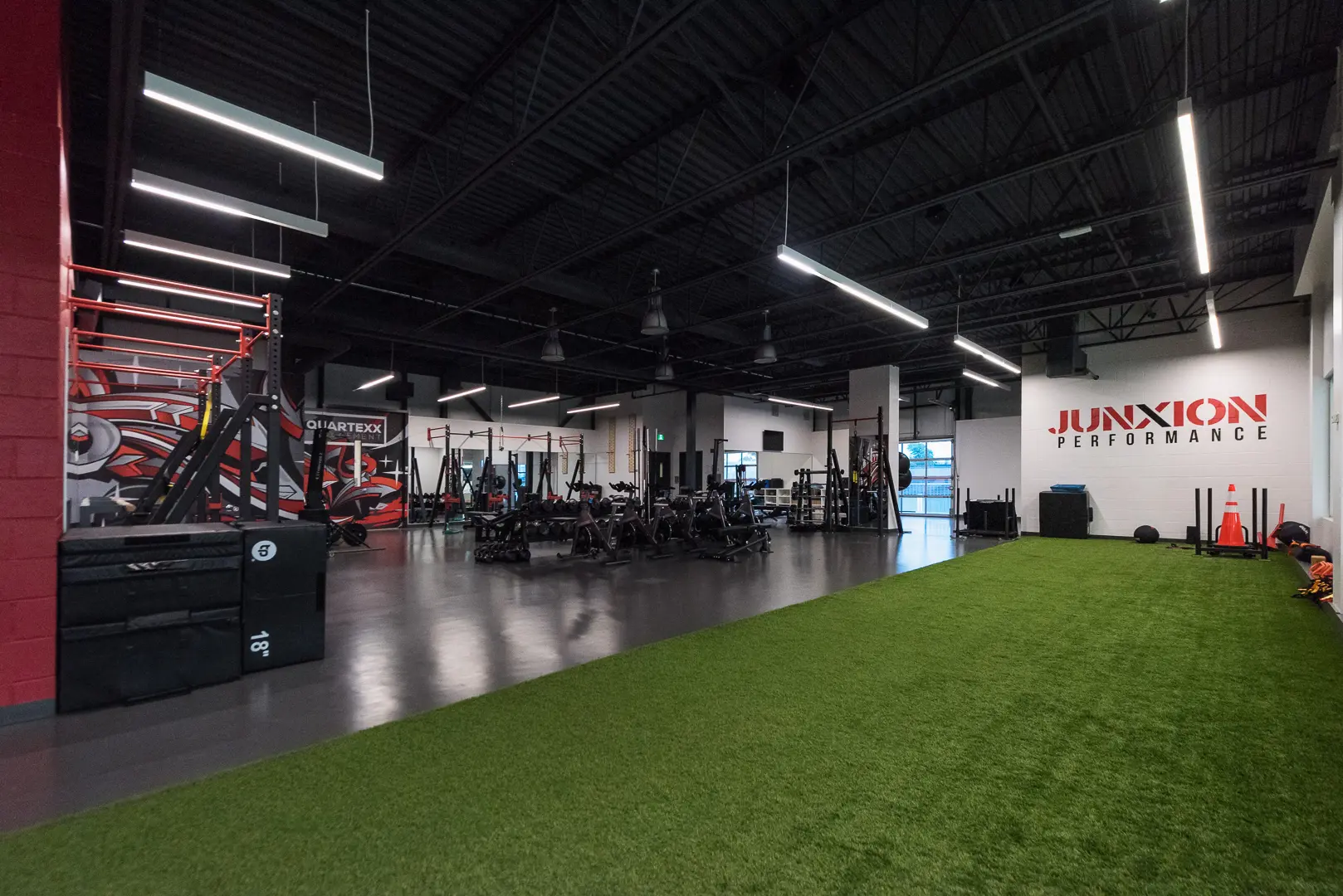 The upstairs gym at JUNXION Performance with a turf area and various gym equipment in the background.