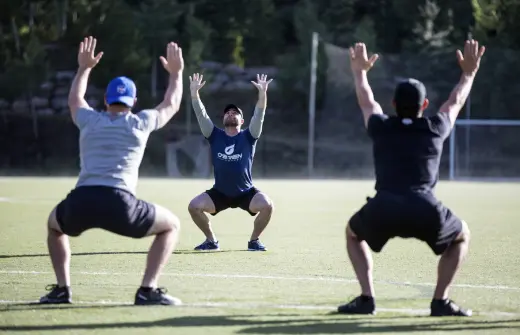 Andy O'Brien squatting with two clients in a soccer field with their arms raised to the sky.